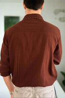 Person wearing a brown shirt from behind with a plain background