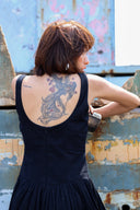 Woman with a tattoo on her back standing against a rustic wall.