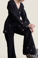 Person wearing a black outfit with colorful heart patterns sitting on a chair.