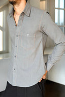 Person wearing a gray button-up shirt with a visible brand logo in an indoor setting.