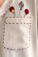 Close-up of a beige fabric with embroidered balloons and a pocket.