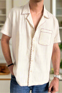 Man wearing a white short-sleeve shirt with red stitching on a beige background