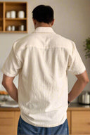 Person wearing a white short-sleeve shirt with a beige background