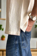 Person wearing a white shirt and blue jeans with a watch on a neutral background