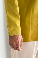 Close-up of a yellow garment with floral embroidery on a neutral background