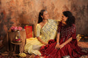 Two women in traditional attire sitting together with a textured wall background