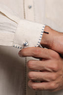 Close-up of a hand adjusting the cuff of a beige jacket with a white shirt underneath.