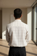 Back view of a person wearing a light gray checkered shirt against a gray background