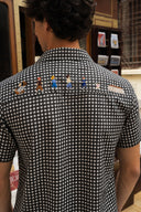 A man viewed from behind wearing a black and white gingham short-sleeve shirt with embroidered cartoon dog characters across the upper back.