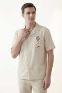 Man wearing a beige shirt with a colorful embroidered design on a white background