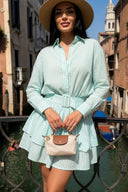 Woman in a light green dress with a hat standing by a canal in an urban setting.