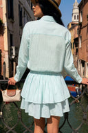 Woman in a light blue outfit standing by a canal with buildings in the background