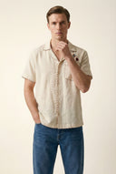 Man wearing a beige short-sleeve shirt and blue jeans on a plain background