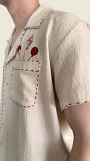 Close-up of a beige shirt with embroidered designs on a plain background