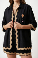 Person wearing a black outfit with beige trim on a white background